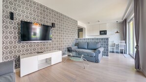 Ett modernt vardagsrum med en platt-TV, ett soffbord i glas och en grå soffa.