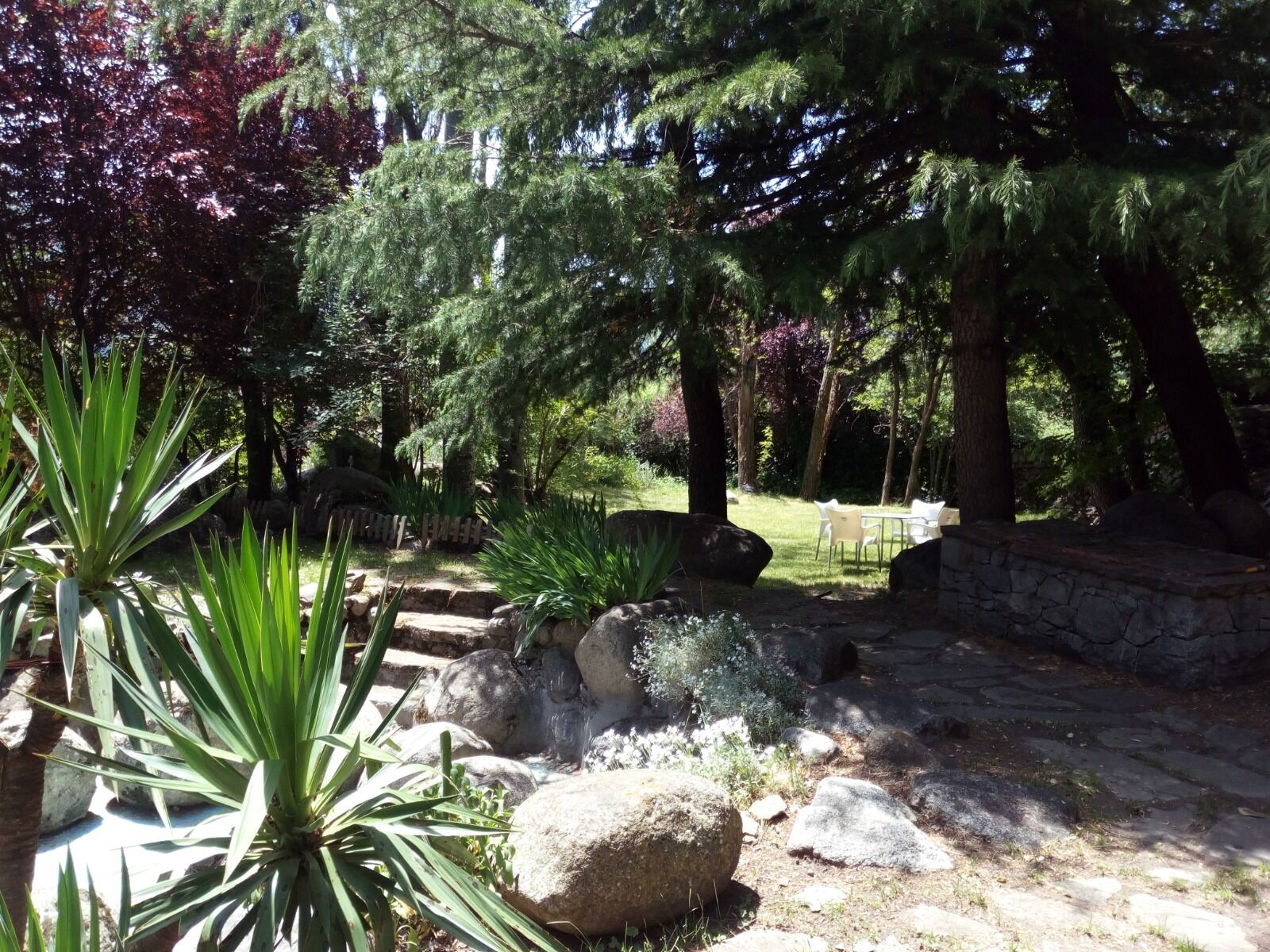 Ein Garten mit großen Steinen, einer Steinmauer und einem Tisch mit Stühlen.