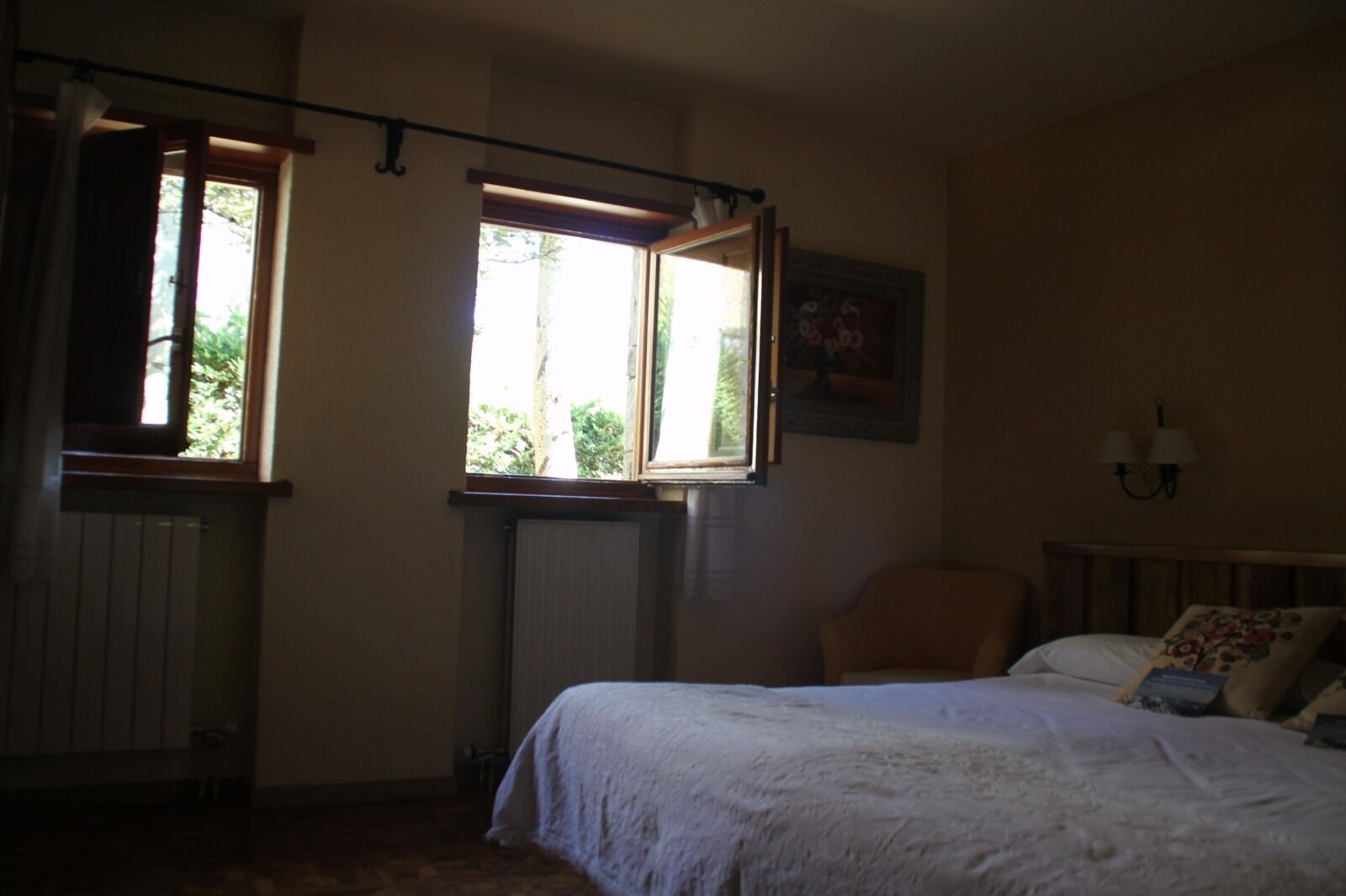 Un dormitorio con cama, una silla, un radiador y dos ventanas.