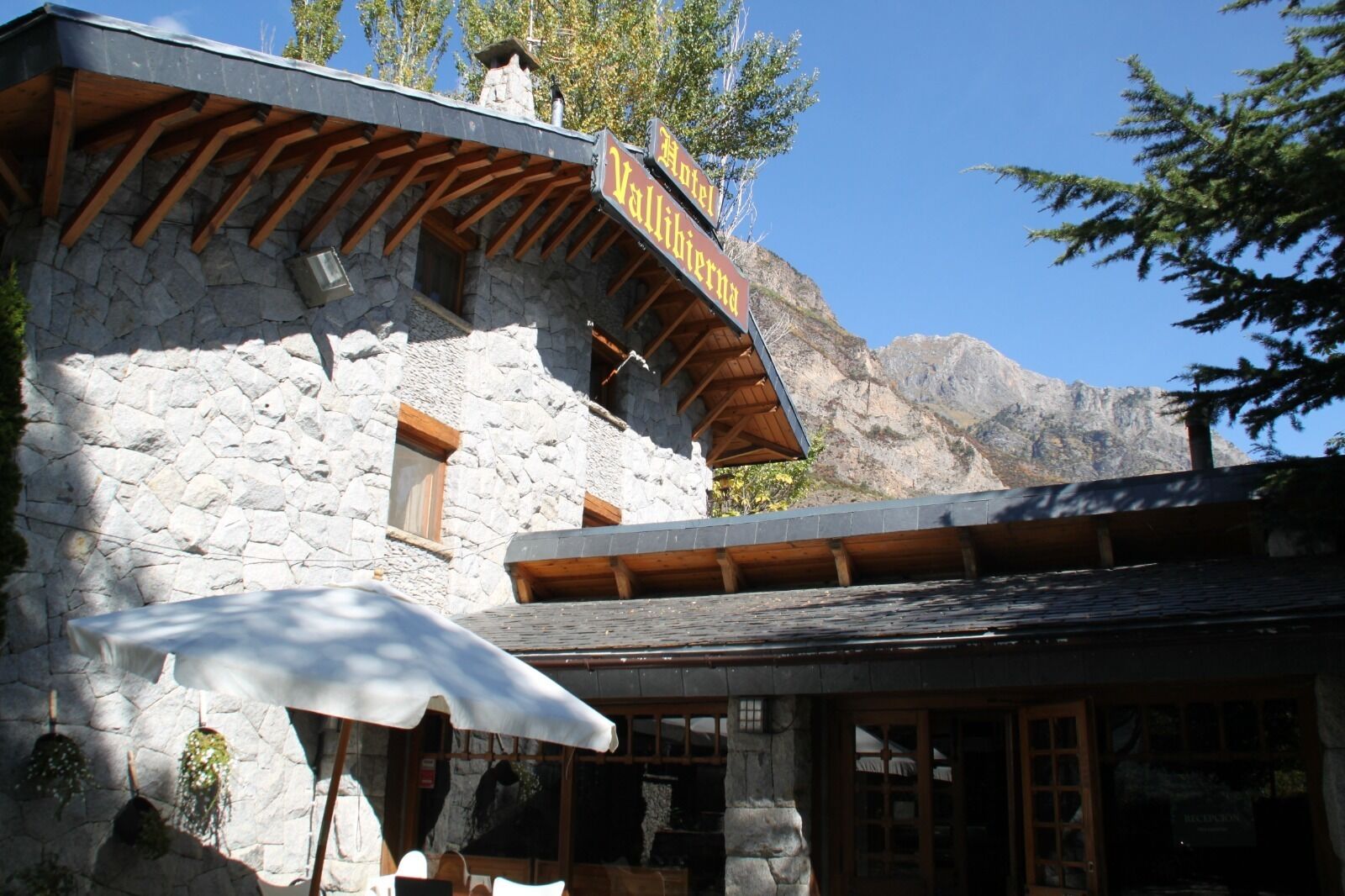 Un edificio de piedra con un balcón de madera, una zona de recepción y montañas al fondo.