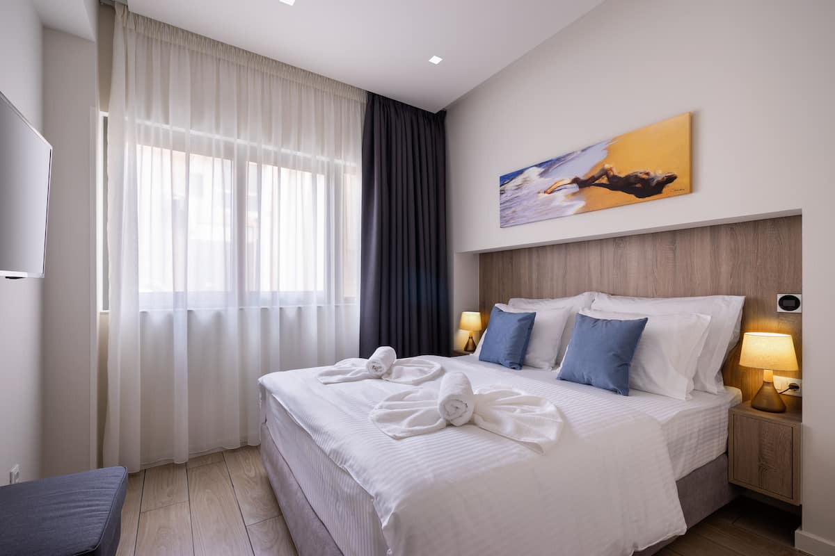Een hotelkamer met een groot bed, twee bedlampen, een schilderij aan de muur en een raam met gordijnen.