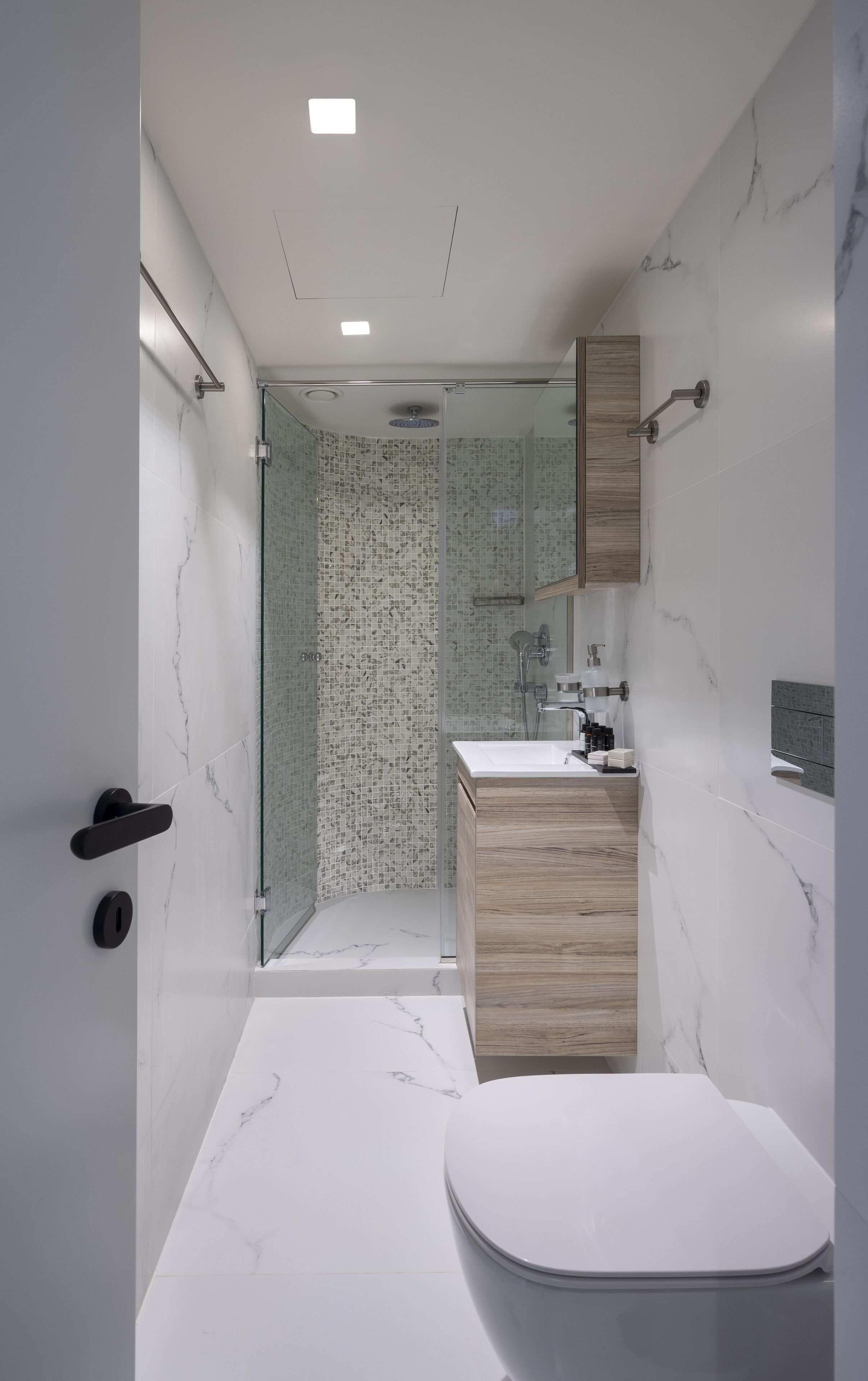 A modern bathroom with a glass shower enclosure, a wooden vanity, and a white toilet.