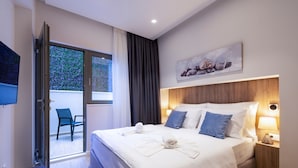 Una habitación de hotel moderna con una cama grande, un televisor de pantalla plana, un cabecero de madera y un cuadro en la pared.