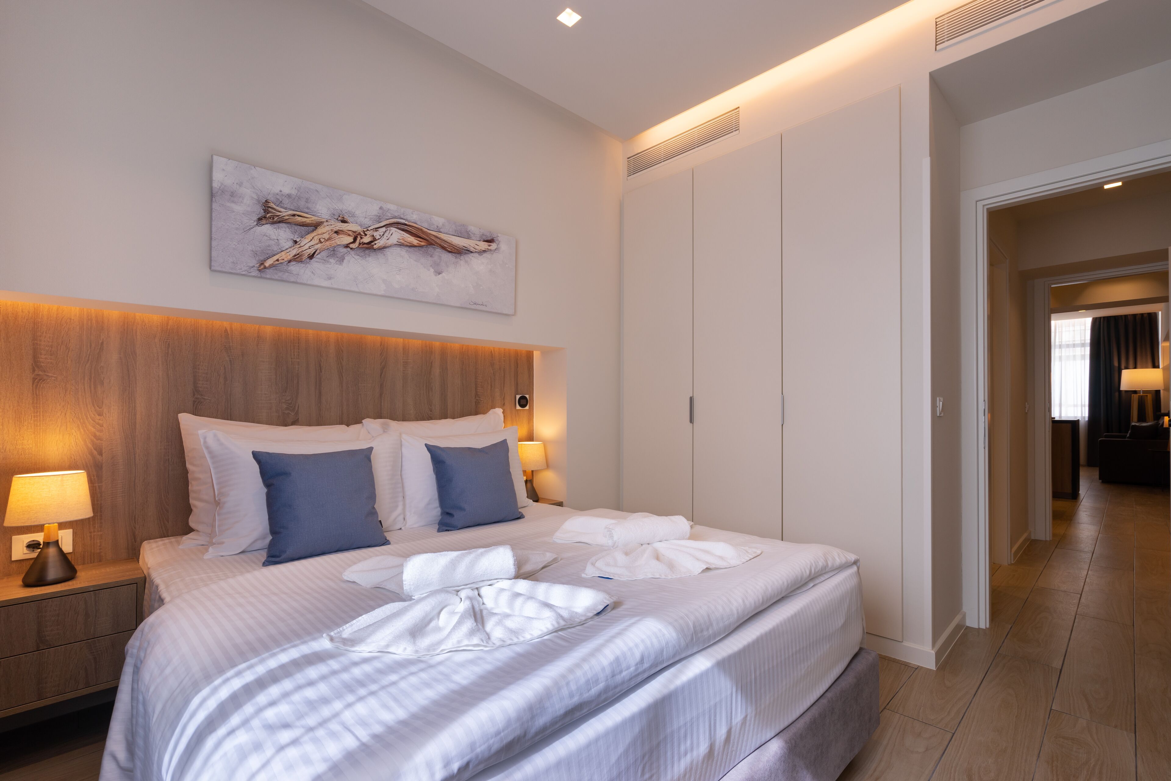 A hotel room with a large bed, a wooden headboard, a bedside table with a lamp, and a painting on the wall.