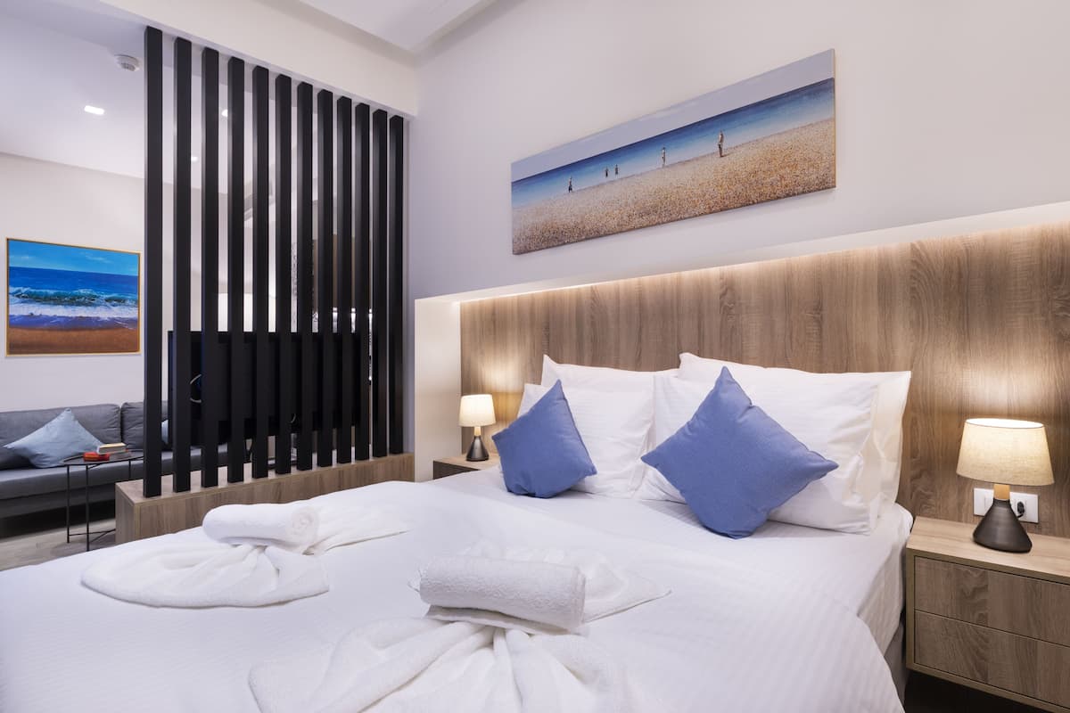 Een hotelkamer met een groot bed, twee kussens, een nachtkastje met een lamp, een houten hoofdeinde, een schilderij van een strandlandschap, een bank en een decoratief scherm.