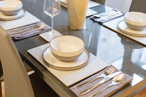 A neatly set dining table with white plates, bowls, and cutlery, and a glass of water.