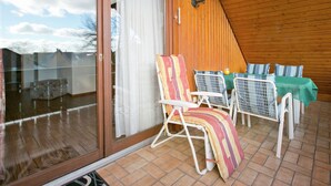 A covered patio with a table and chairs, a sliding glass door, and a wooden ceiling. - Spacious Apartment near Lake Constance with Covered Balcony (Bermatingen)