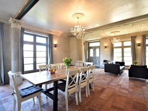 A spacious dining area with a large wooden table, white chairs, and a chandelier. There are two black sofas in the background, and the room has large windows with curtains. - Stilvolles Ferienhaus in Detershagen mit Garten (Kroepelin)