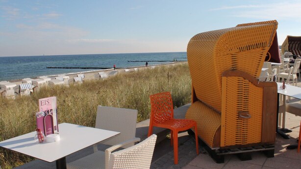 Een restaurant aan het strand met terras, uitzicht op de zee en een bordje met 'EIS'.