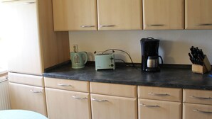 Una cocina con armarios de madera clara, encimera negra, hervidor, tostadora, cafetera y bloque de cuchillos.