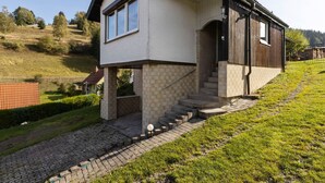 Ein modernes, zweistöckiges Haus mit Satteldach, einer sichtbaren Treppe zum Eingang und einer gepflasterten Auffahrt.