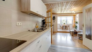 Eine moderne Küche mit Einbauherd, Kaffeemaschine und Spüle. Durch einen offenen Durchgang ist ein Essbereich mit Tisch und Stühlen zu sehen.