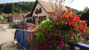 A building with a sloped roof, a visible entrance, and a blue fence in the foreground. - Family Escape With Garden (Saint-Quirin)