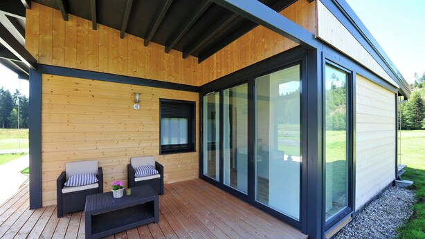 A modern building with a wooden deck, two chairs, a table, and large sliding glass doors. - Family Escape With Garden (Saint-Quirin)