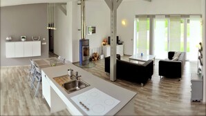 A modern kitchen with a central island, a dining area with black sofas, and a large window providing a view of the outdoors. - Family Escape With Garden (Saint-Quirin)