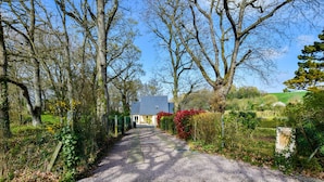 Un chemin de gravier mène à une maison entourée d’arbres et de verdure.