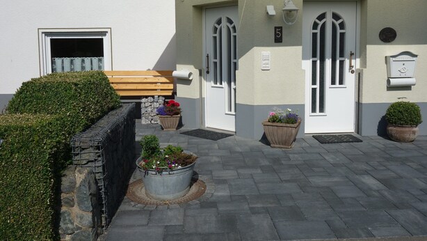 A building with a white exterior, a wooden bench, and potted plants. - Ferienwohnung im Ennerichtal (Runkel)