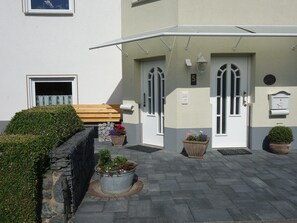 A building with a white exterior, a wooden bench, and potted plants. - Ferienwohnung im Ennerichtal (Runkel)