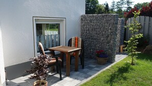 An outdoor patio with a table and chairs, a potted plant, and a stone wall. - Ferienwohnung im Ennerichtal (Runkel)