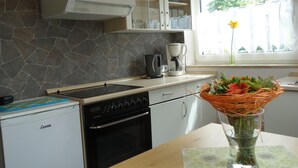 A kitchen with a stone backsplash, a coffee maker, and a vase with flowers on the counter. - Ferienwohnung im Ennerichtal (Runkel)