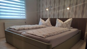 A modern bedroom with a bed, two pillows, a bedside table, and a wall-mounted light fixture. - Ferienwohnung im Ennerichtal (Runkel)