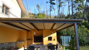 A covered outdoor patio with a table and chairs, a built-in grill, and potted plants. - Modern Poolside Home in Pescia (Pescia)