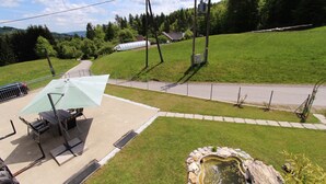 Une terrasse avec une table et des chaises, un petit étang et une route en arrière-plan.