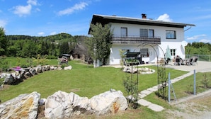 Une maison à deux étages dotée d’un balcon, entourée d’une pelouse bien entretenue et de murs en pierre.