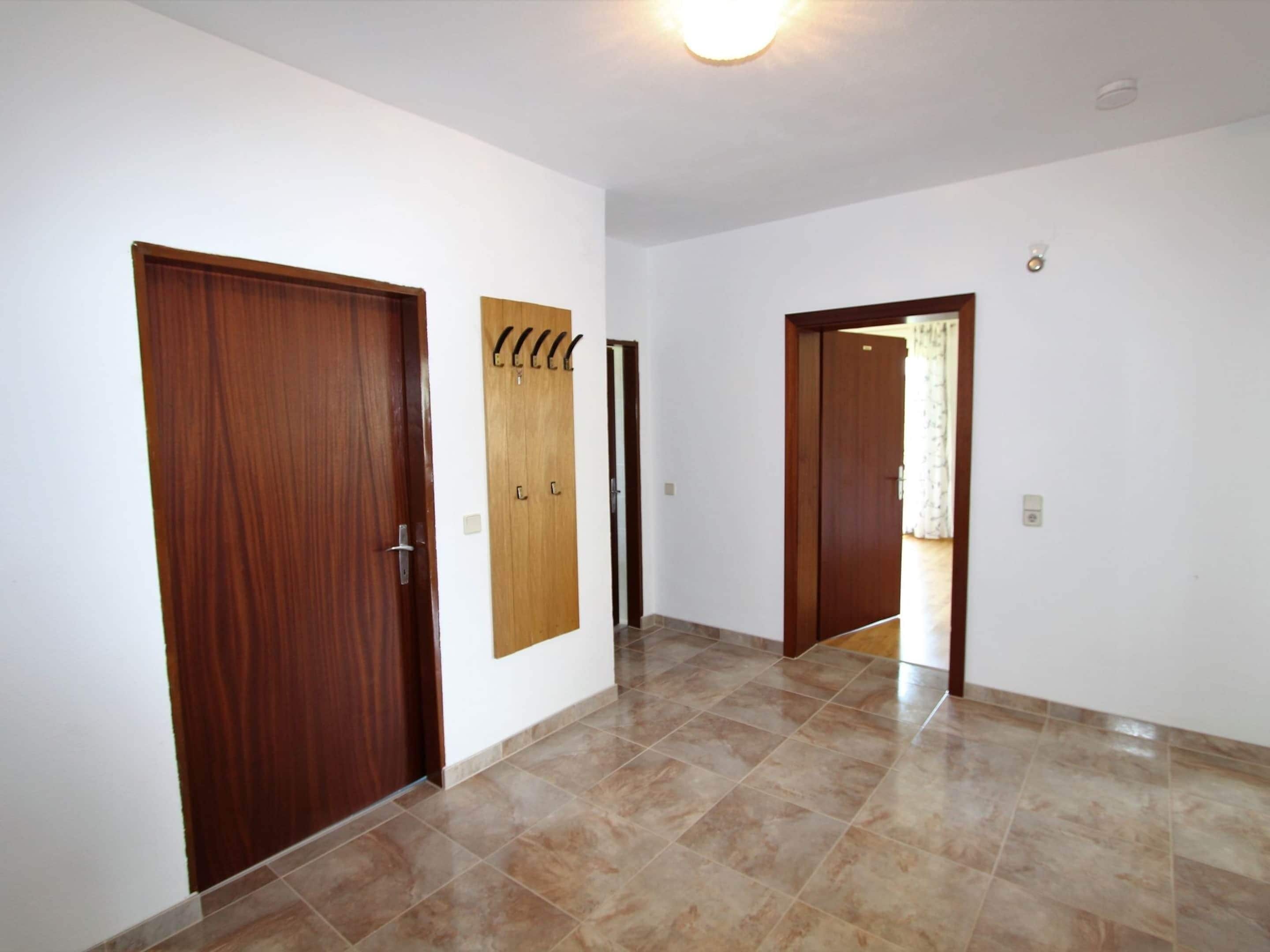A hallway with two wooden doors, a coat rack, and a tiled floor.