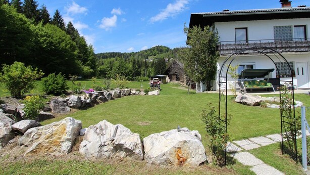 Un bâtiment blanc doté d’un balcon, entouré d’une pelouse bien entretenue et de gros rochers.
