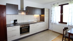 Une cuisine moderne équipée d’un four encastré, d’un évier et d’une cuisinière. Il y a une fenêtre avec des rideaux et une chaise près de la fenêtre.