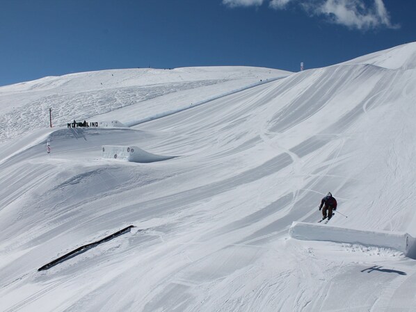Ein verschneiter Skiabhang mit markierten Pisten und einem Skifahrer in Bewegung.