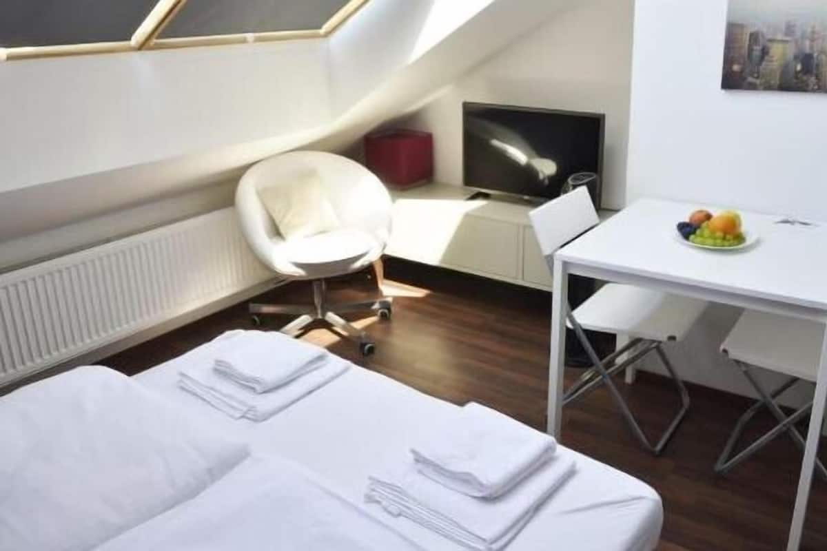 A modern hotel room with a skylight, a bed, a desk, a chair, a television, and a fruit bowl.