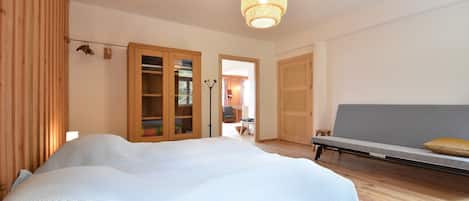 A bedroom with a bed, wooden wardrobe, and a bench with cushions.