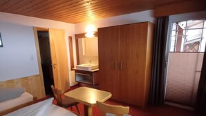 Hotellihuone, jossa on kaksi erillistä sänkyä, pieni pöytä ja tuoli, puinen vaatekaappi, kylpyhuone, jossa on pesuallas ja peili, sekä ikkuna, josta on näkymä.