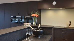 A modern kitchen with dark cabinetry, a built-in oven, and a countertop with a vase of flowers and champagne glasses. - Luxurious Apartment in Nieuwpoort with Hot Tub (Nieuwpoort)