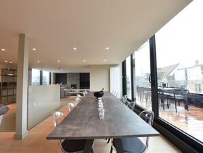 A modern dining area with a long table, clear chairs, and a view of the city through large windows. - Luxurious Apartment in Nieuwpoort with Hot Tub (Nieuwpoort)