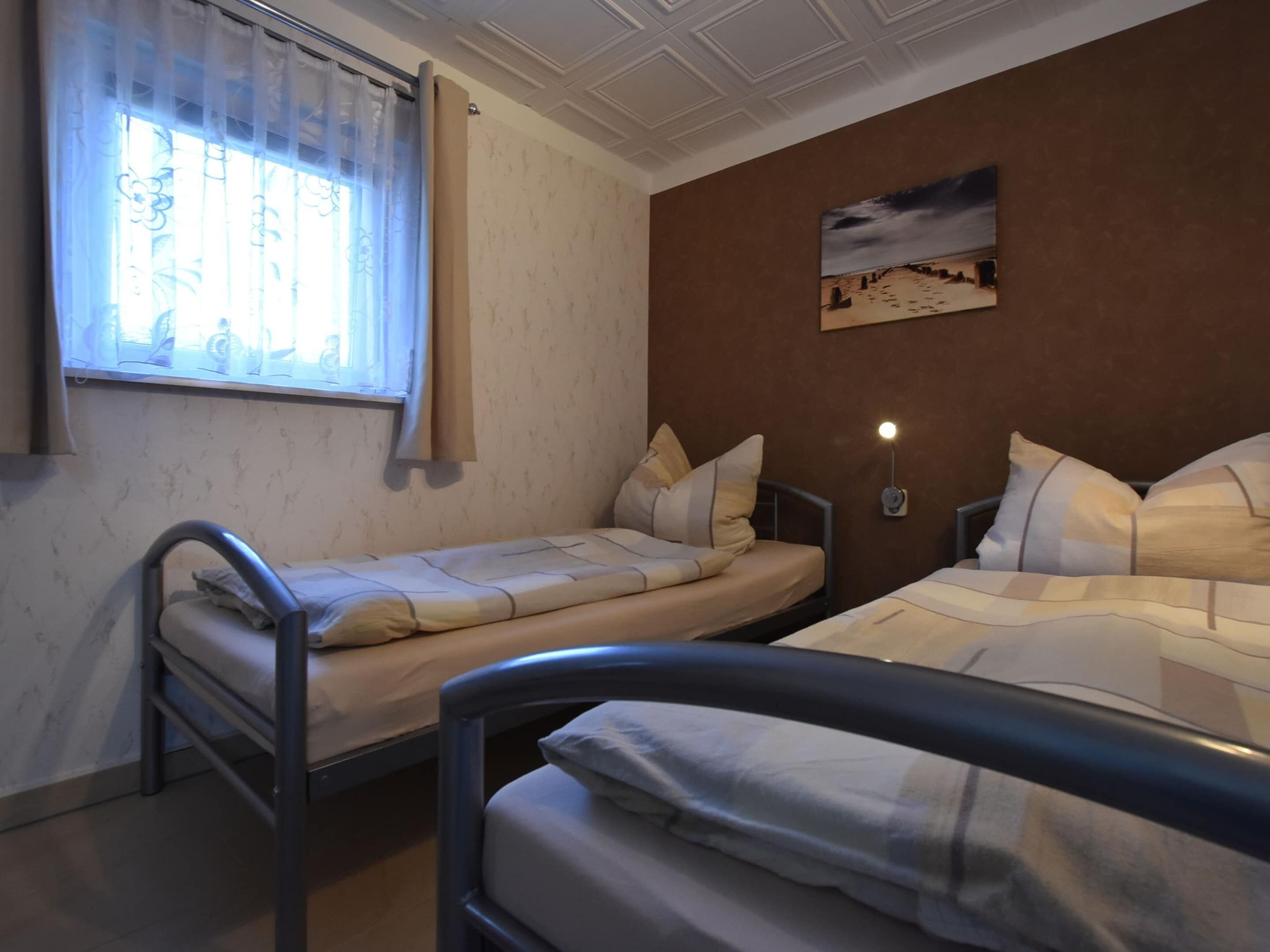 Une chambre avec deux lits simples, une fenêtre avec des rideaux, un tableau accroché au mur et une lampe de chevet.