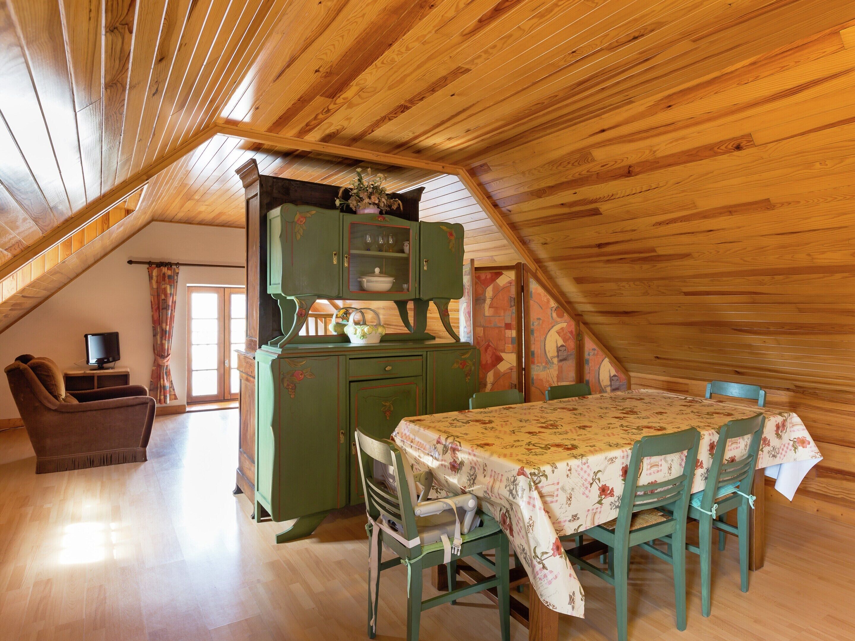Un coin repas avec une table dressée pour quatre personnes, un buffet vert aux portes vitrées et un téléviseur placé dans un coin.
