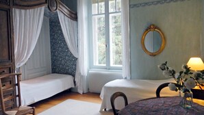 A bedroom with two single beds, a wooden chair, a round table with a vase of flowers, a mirror, and a window with curtains. - Mansion in Vecoux With Pool and Garden (Vecoux)