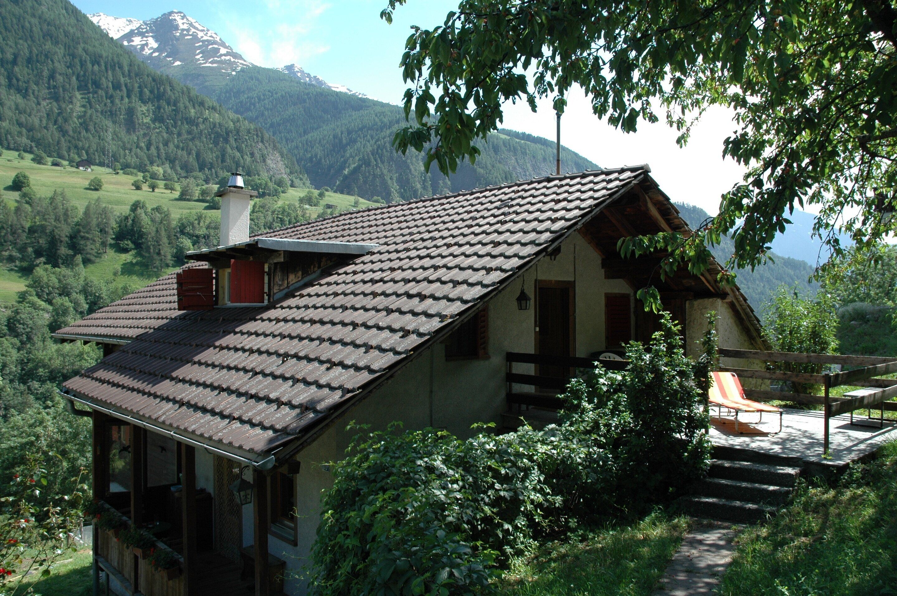 Une maison de montagne avec un toit en pente, une cheminée et un balcon donnant sur une vallée.