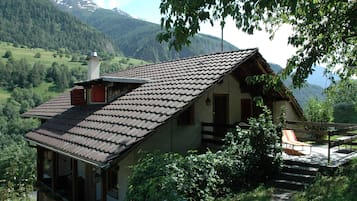 Une maison de montagne avec un toit en pente, une cheminée et un balcon donnant sur une vallée.