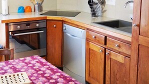 A kitchen with wooden cabinets, a clock, a sink, and a table with a floral tablecloth. - Chalet in La Bresse Near Ski Slopes (Le Menil)