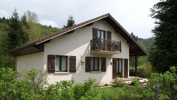 A two-story house with a balcony, surrounded by greenery and hills. - Chalet in La Bresse Near Ski Slopes (Le Menil)