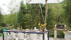 An outdoor dining area with a table set for six, surrounded by white plastic chairs, a grill, and a white umbrella. - Chalet in La Bresse Near Ski Slopes (Le Menil)