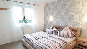 A bedroom with a wooden bed, striped bedding, a nightstand, a window with curtains, and a radiator.