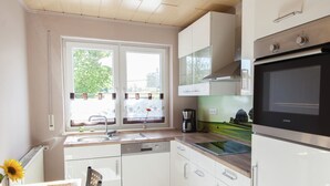 A modern kitchen with white cabinets, a stainless steel oven, a coffee maker, and a window with a view of greenery.