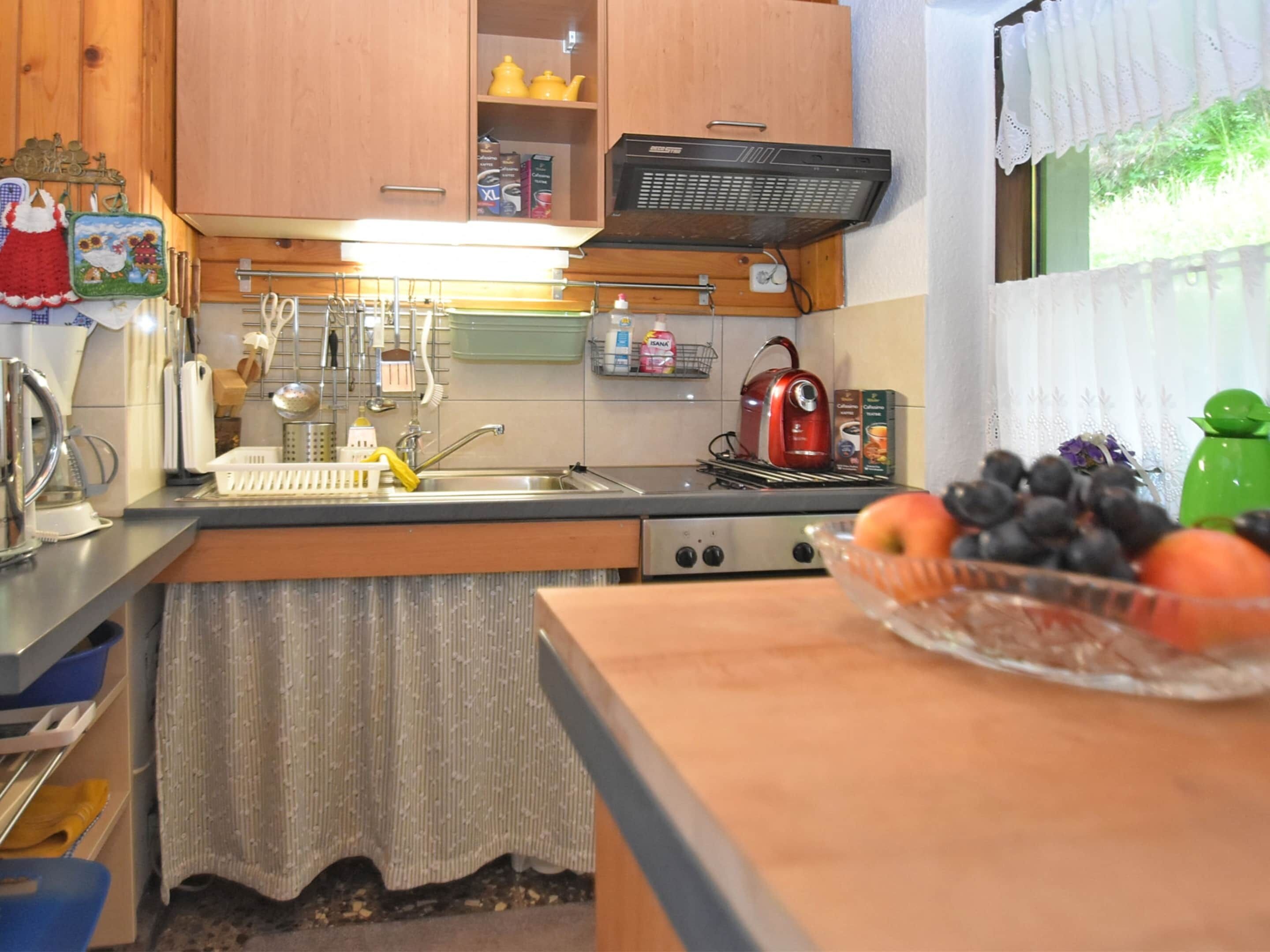 A kitchen with wooden cabinets, a stove, a sink, and a window with a curtain.