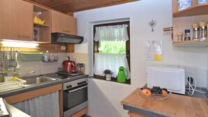 Cozinha compacta com armários de madeira, fogão, pia e janela com cortina de renda.