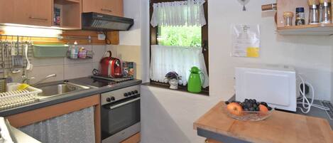 A compact kitchen with wooden cabinets, a stove, a sink, and a window with a lace curtain.